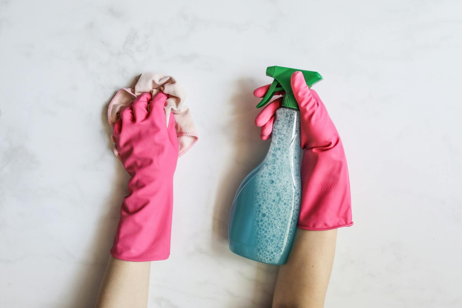 Gloved hands cleaning a surface with spray and cloth