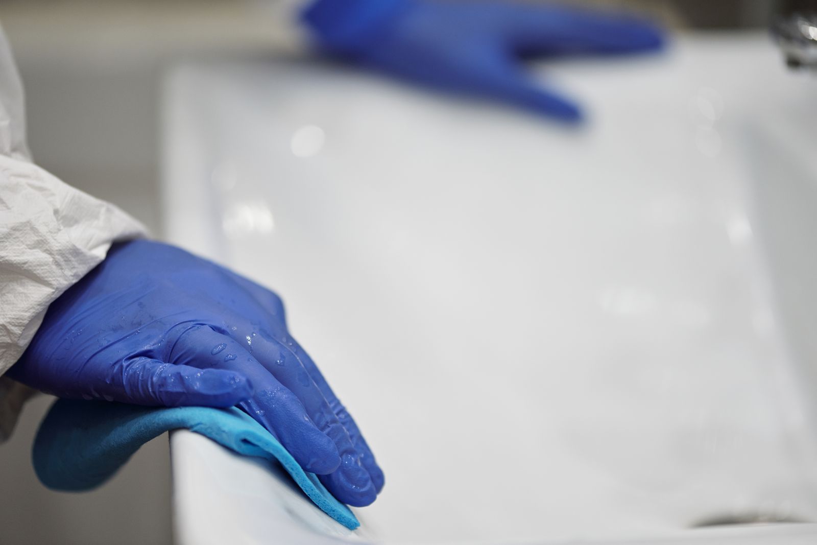 Gloved hands cleaning a bathroom sink after contamination