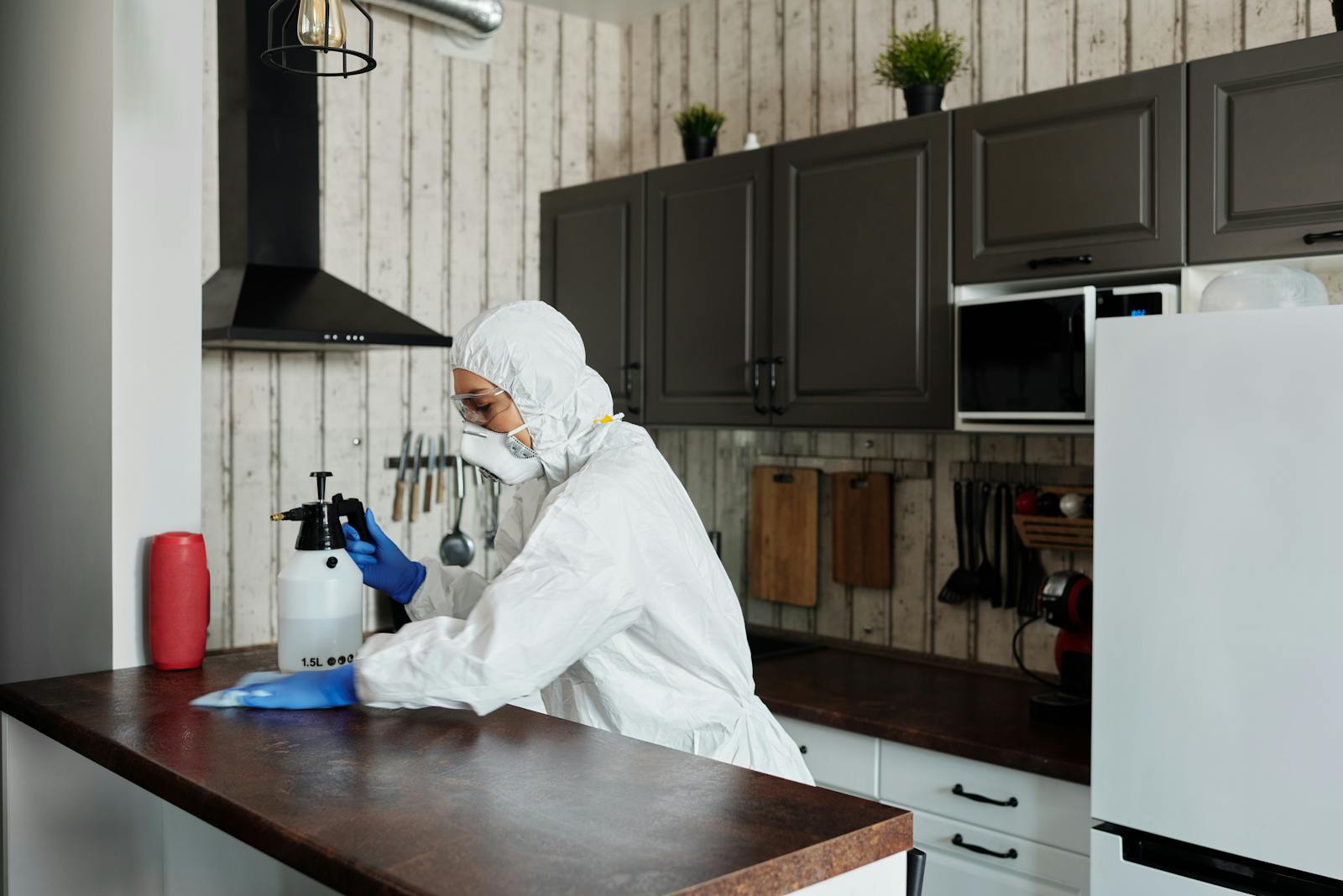 Specialist cleaner in protective suit disinfecting a kitchen counter