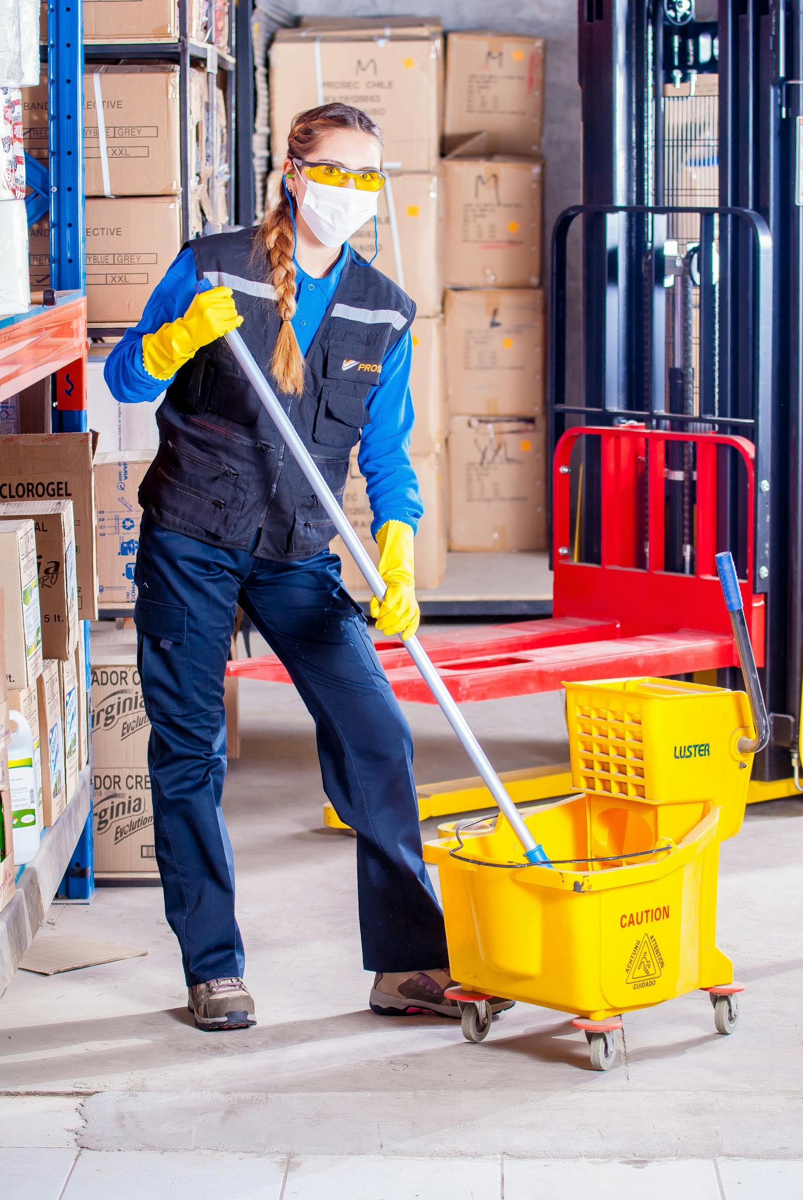 Cleaner mopping a warehouse floor with safety equipment