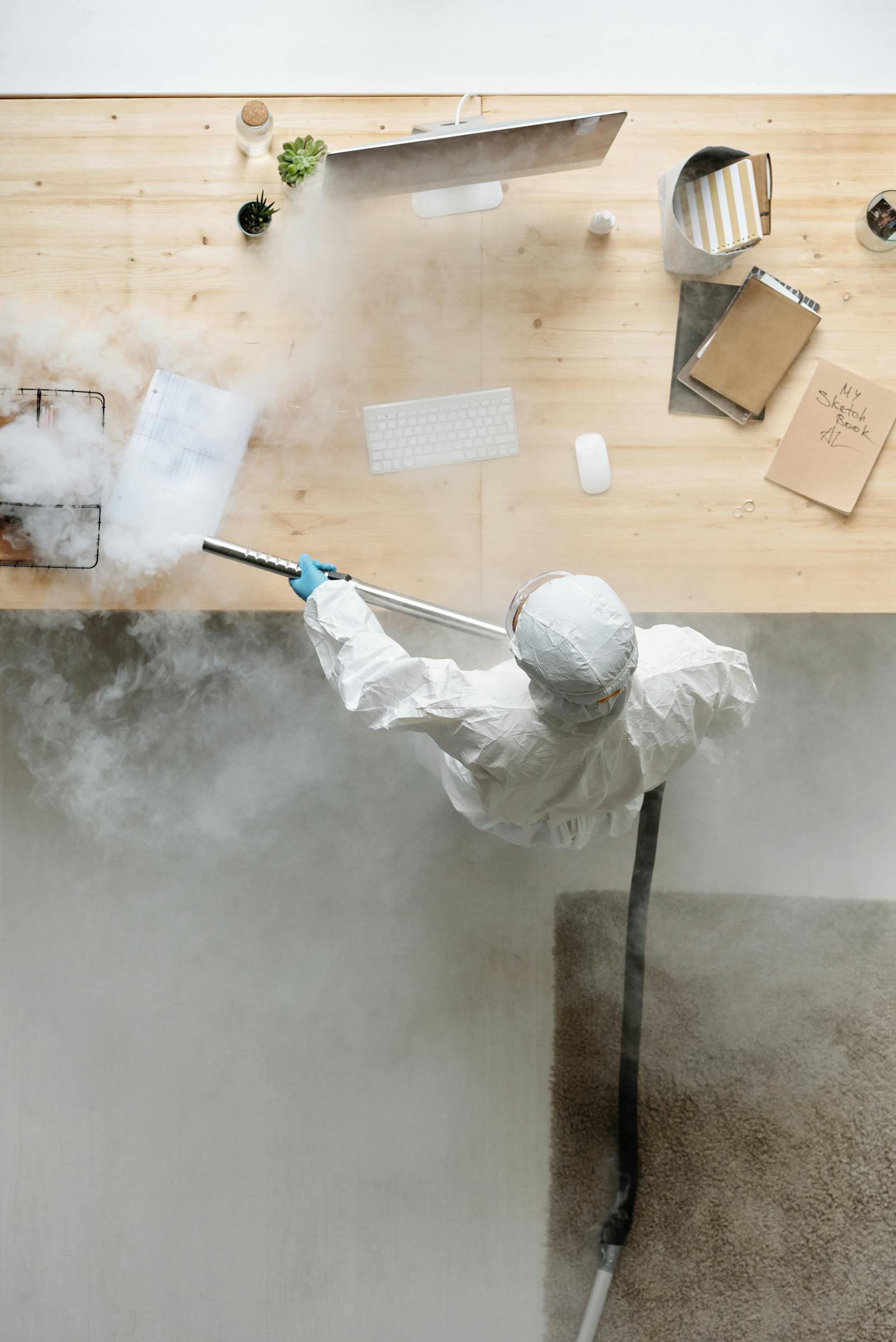 Cleaner in protective equipment disinfecting an office desk