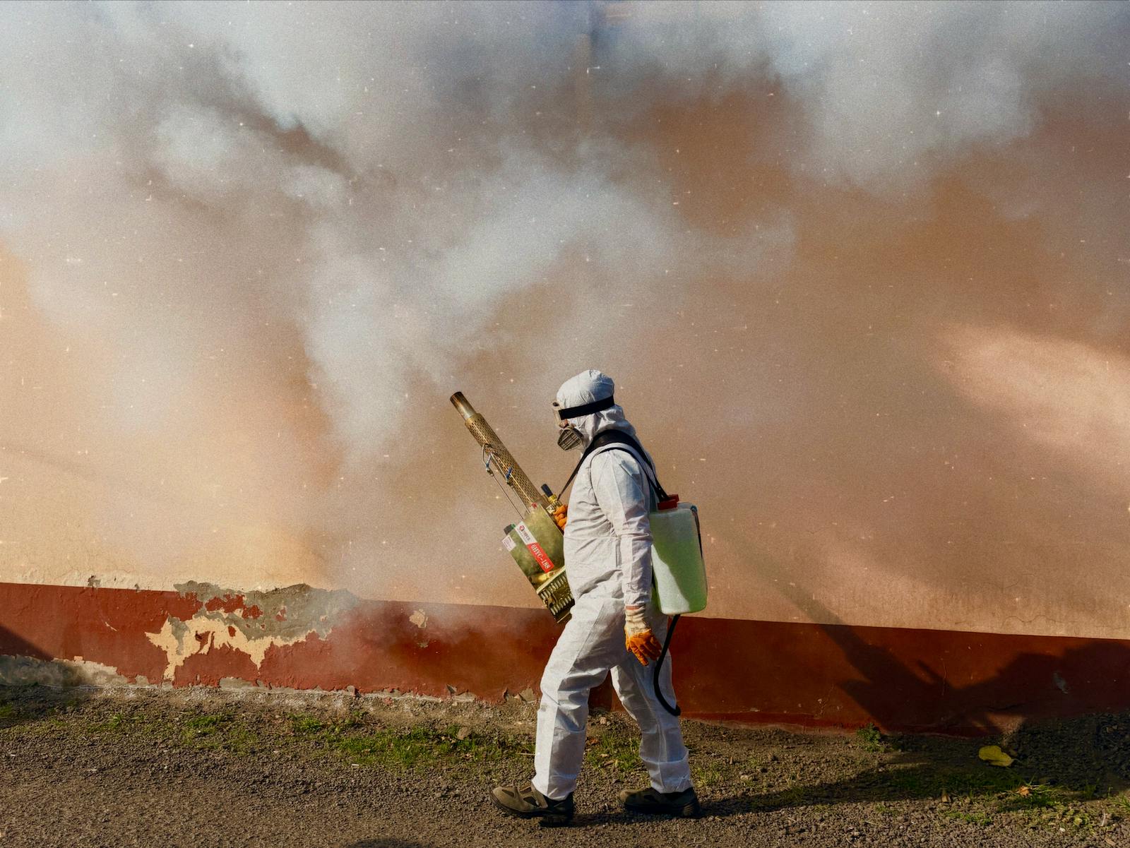 Pest control worker in protective suit treating an outdoor area