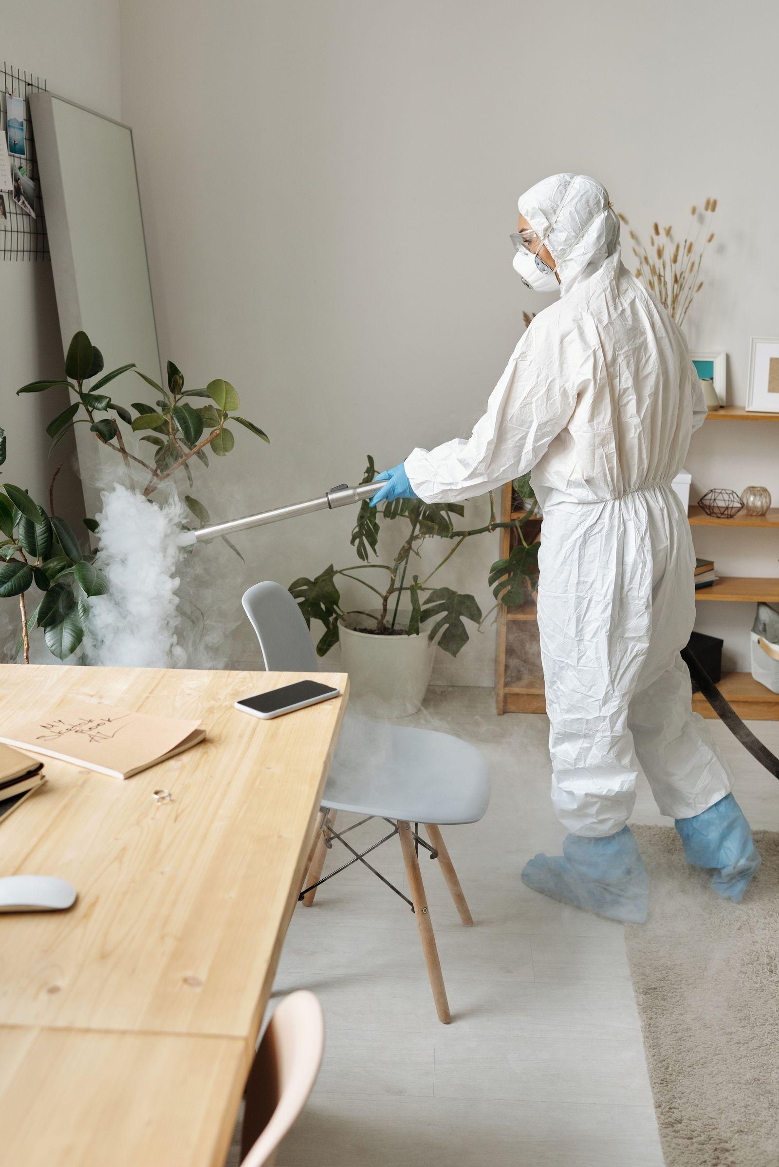 Cleaner in protective clothing disinfecting an office workspace