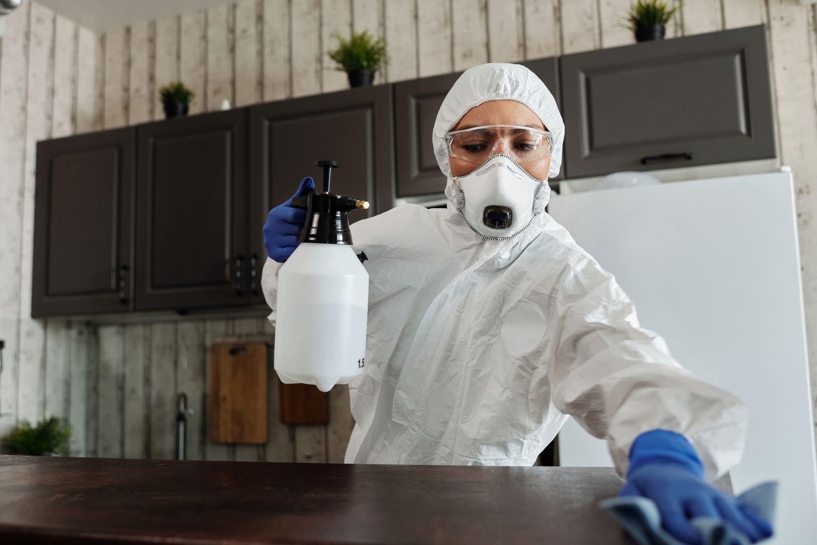 Cleaner wearing protective clothing, gloves and a respirator wiping a surface